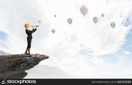 Young woman engineer on rock top looking in spyglass. Searching for perspectives