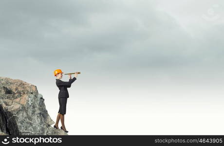 Young woman engineer on rock top looking in spyglass. Searching for perspectives