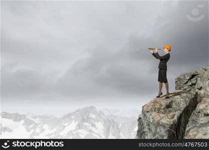 Young woman engineer on rock top looking in spyglass. Searching for perspectives