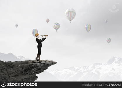 Young woman engineer on rock top looking in spyglass. Searching for perspectives