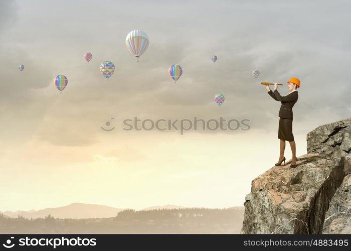 Young woman engineer on rock top looking in spyglass. Searching for perspectives