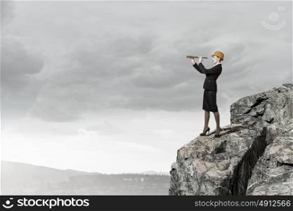 Young woman engineer on rock top looking in spyglass. Searching for perspectives