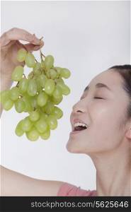 Young woman enjoying a bunch of grapes raised above her head, studio shot