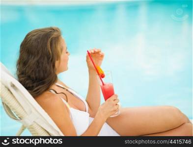Young woman enjoying cocktail at poolside. rear view