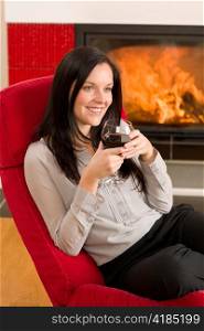 Young woman enjoying glass of red wine by home fireplace