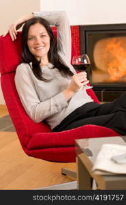 Young woman enjoying glass of red wine by home fireplace