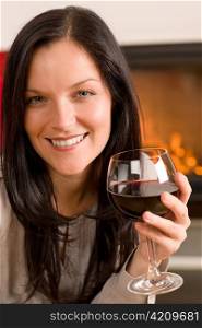 Young woman enjoying glass of red wine by home fireplace