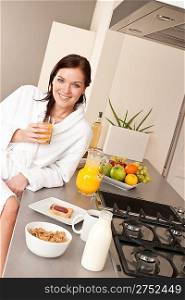 Young woman enjoying orange juice and breakfast in modern kitchen