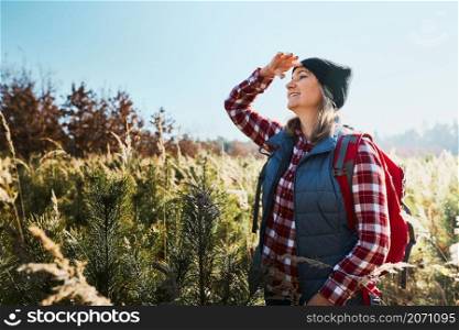 Young woman enjoying the view of mountains. Woman standing on trail and looking at view. Woman with backpack hiking through tall grass along path in mountains. Spending summer vacation close to nature