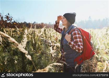 Young woman enjoying the view of mountains. Woman standing on trail and looking at view. Woman with backpack hiking through tall grass along path in mountains. Spending summer vacation close to nature