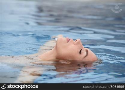 Young woman enjoying water and sun in outdoor swimming pool. Woman enjoying water