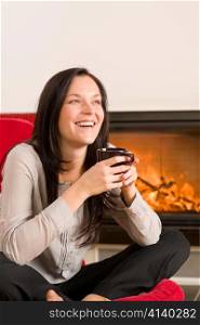 Young woman enjoying winter hot drink by home fireplace