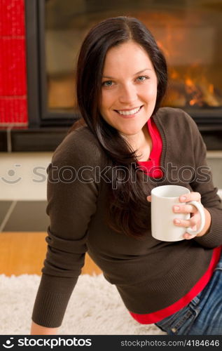 Young woman enjoying winter hot drink by home fireplace