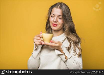 young woman enjoys smell her fresh coffee against yellow background