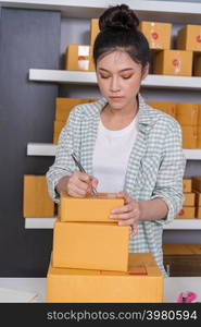 young woman entrepreneur writing on parcel box, online business, prepare before delivery