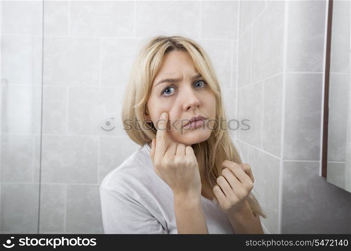 Young woman examining pimples on face in bathroom