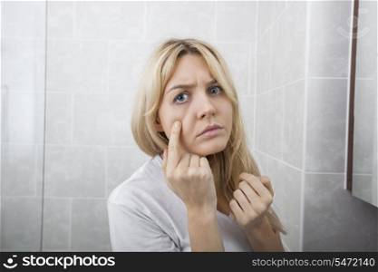 Young woman examining pimples on face in bathroom