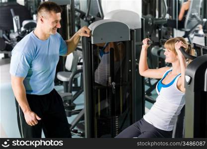 Young woman exercise on shoulder press machine with personal trainer