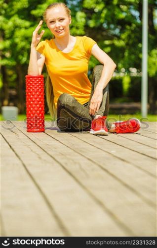 Young woman exercises in park, using gym accessory, foam roller for muscle massage. Staying fit and healthy.. Girl doing exercises outdoor, using roller