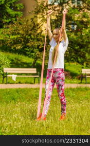Young woman exercises outdoor in park, using gym accessory, resistance band. Staying fit and healthy.. Girl doing exercises outdoor, using resistance fit band.