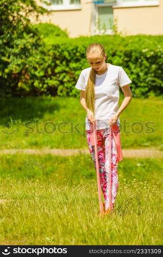 Young woman exercises outdoor in park, using gym accessory, resistance band. Staying fit and healthy.. Girl doing exercises outdoor, using resistance fit band.