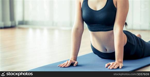 Young woman exercising in indoor gym on yoga mat. Healthy lifestyle and wellness concept.
