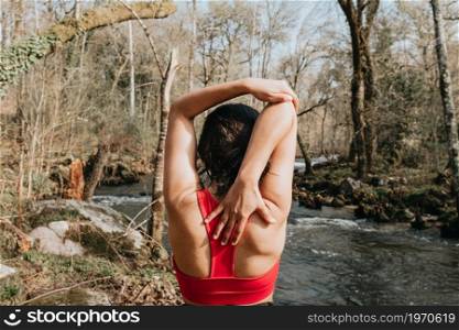 Young woman exercising in sport clothes in the middle of the forest during an autumnal day with a river, with copy space