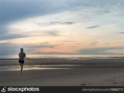 Young woman exercising on the sea beach at sunrise. Back view, Copy space, Selective focus.