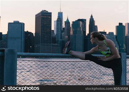 Young woman exercising outdoors, stretching by waterfront, Brooklyn, New York, USA