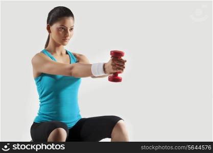Young woman exercising with dumbbells isolated over gray background