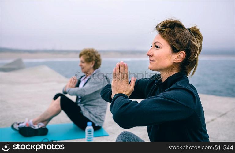 Young woman exercising with elderly woman in a concrete pier. Women exercising in a concrete pier