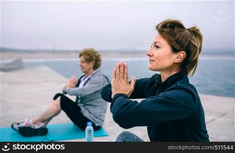 Young woman exercising with elderly woman in a concrete pier. Women exercising in a concrete pier