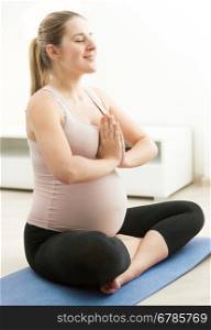 Young woman expecting baby practicing yoga on fitness mat at home