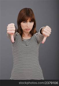 Young woman expressing negativity with thumb down over a grey background