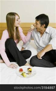 Young woman feeding cake to a mid adult man