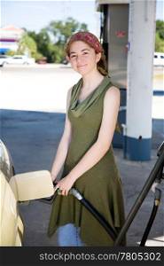 Young woman filling up her gas tank is smiling because she drives a fuel efficient car.