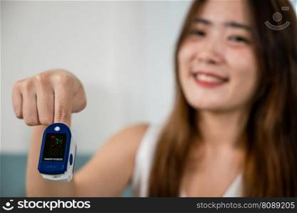 Young woman finger inserted into the pressure oximeter to assess health under sofa in living room at home, Self healthcare with corona virus pandemic, medical health care concept