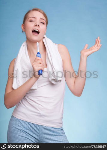 Young woman funny girl singing to toothbrush brushing her white teeth doing fun on blue. Daily dental care. Studio shot.