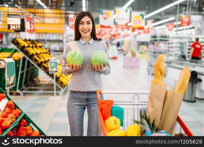 Young woman funs with cabbage swings in a supermarket, family shopping. Customer in shop, buyer in market