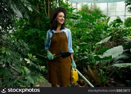 Young woman gardener working in botanic garden. Millennial girl florist walking through lush green plants in greenhouse. Young woman gardener working in botanic garden