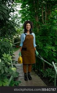 Young woman gardener working in botanic garden. Millennial girl florist walking through lush green plants in greenhouse. Young woman gardener working in botanic garden
