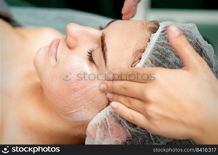 Young woman getting facial massage with closed eyes by beautician in beauty salon. Young woman getting facial massage