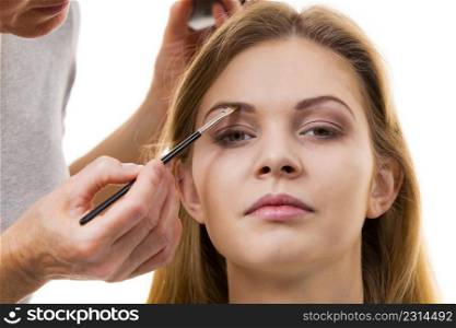 Young woman getting her eyebrow make up done by professional visage artist. Person using brush to paint eyebrows.. Woman getting eyebrows make up done