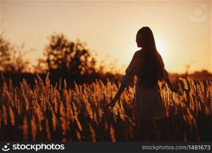 Young woman Girl in field in Sunset in spring, summer landscape background Springtime Summertime. Beautiful smiling woman in a field at sunset. selective focus.. Young woman Girl in field in Sunset in spring, summer landscape background Springtime Summertime. Beautiful smiling woman in a field at sunset. selective focus