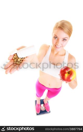 Young woman girl standing on weighing scale holding pills and apple. Choice between synthetic vitamins natural. Health care. Healthy lifestyle nutrition concept. Isolated on white background. . Woman holding vitamins and apple. Health care.