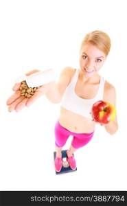 Young woman girl standing on weighing scale holding pills and apple. Choice between synthetic vitamins natural. Health care. Healthy lifestyle nutrition concept. Isolated on white background. . Woman holding vitamins and apple. Health care.