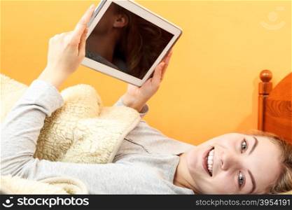 Young woman girl with tablet browsing internet.. Lazy young woman using computer tablet browsing internet. Girl laying in bed under blanket and holding ebook. Technology leisure.