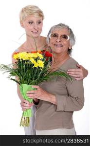 Young woman giving a senior lady a bunch of flowers