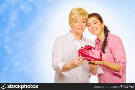 Young woman giving gift to her mother on winter background