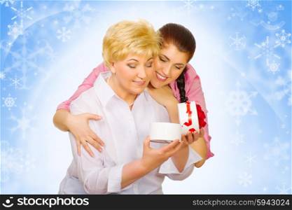Young woman giving gift to her mother on winter background